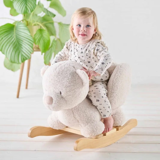 Child sitting on a plush rocking horse toy with a plant in the background
