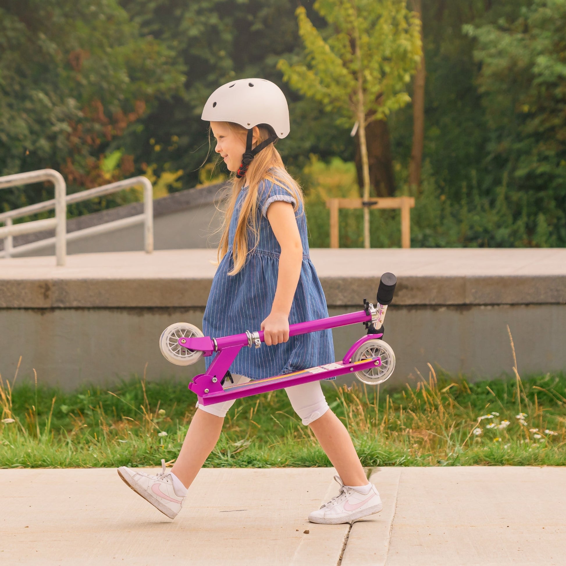 Young girl with a pink scooter walking outdoors on a path.