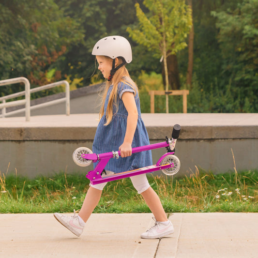 Young girl with a pink scooter walking outdoors on a path.