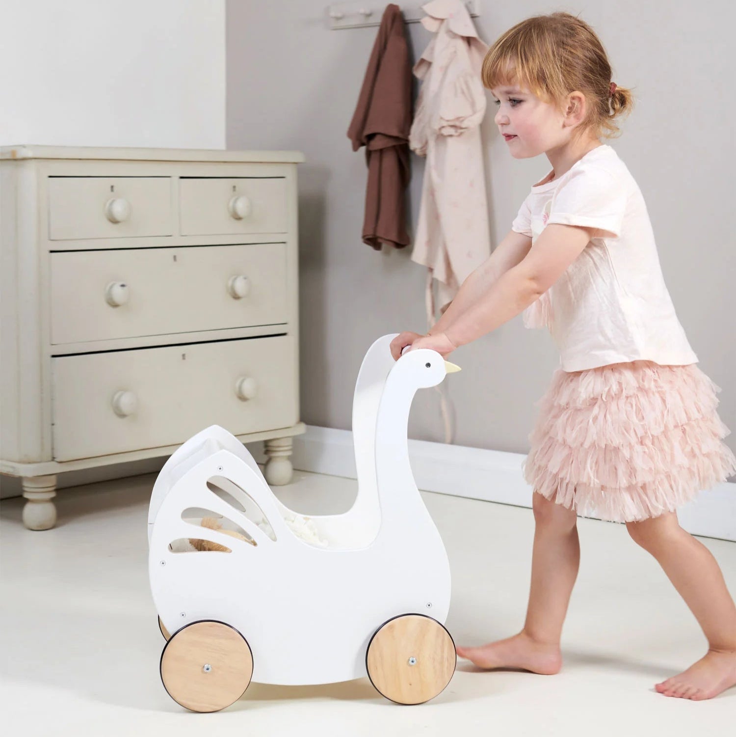 Child playing with a white goose-shaped toy in a room with a dresser and clothes in the background.