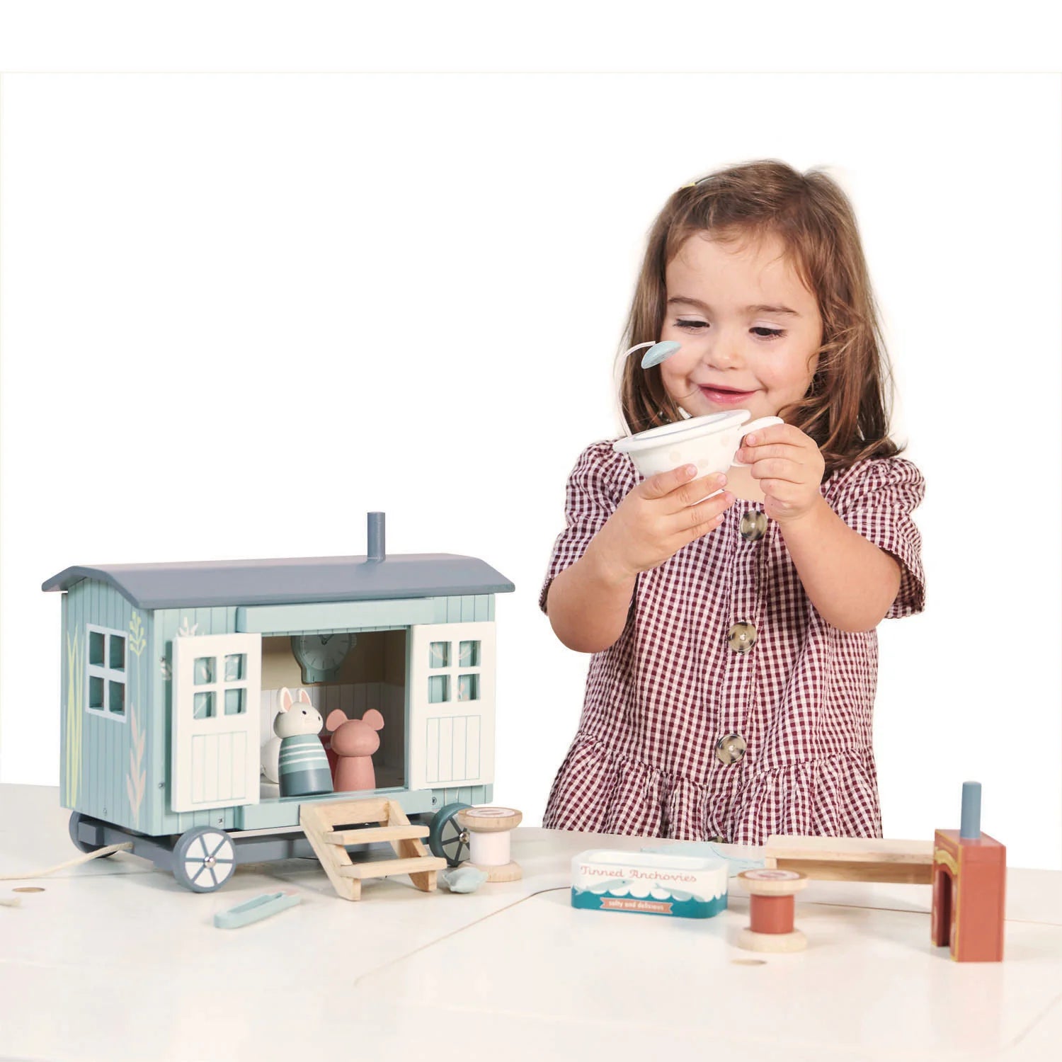 Child playing with a toy wooden house and accessories on a white background
