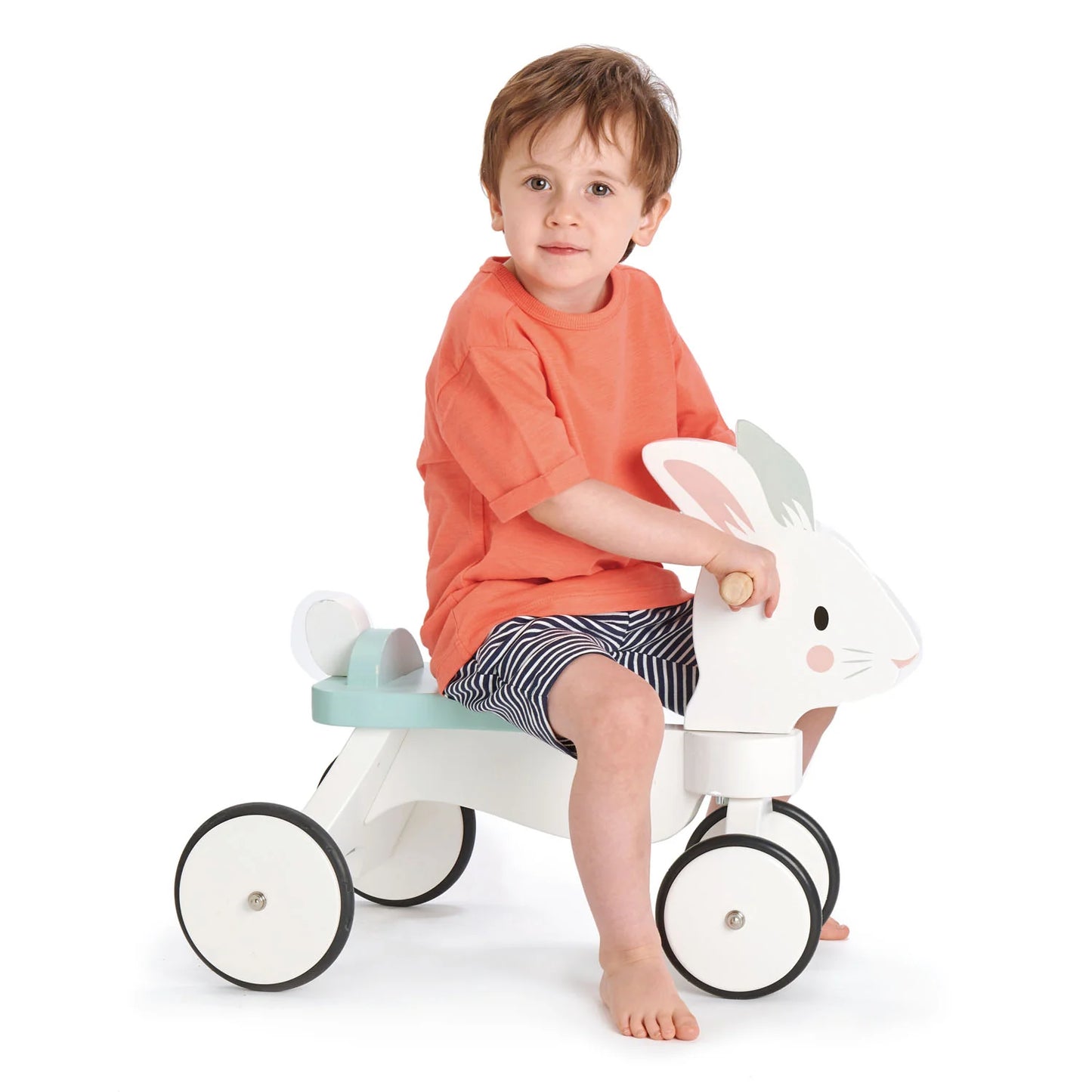 Child sitting on a white toy rabbit with black wheels on a white background