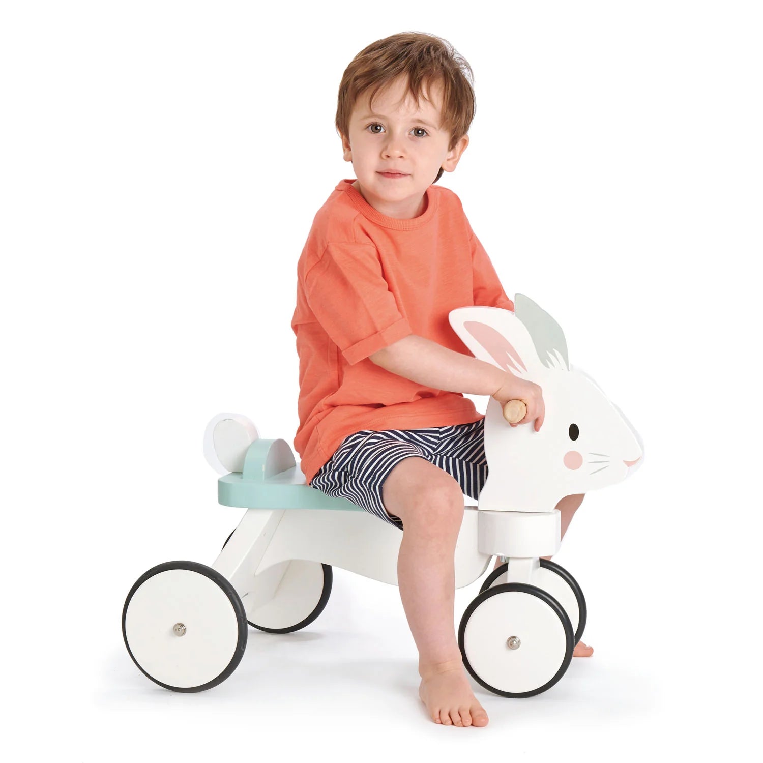 Child sitting on a white toy rabbit with black wheels on a white background