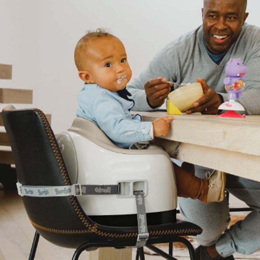 Man and child sitting at a table with a high chair, eating together.