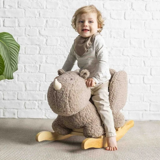 Child holding a plush rhino toy on a soft surface