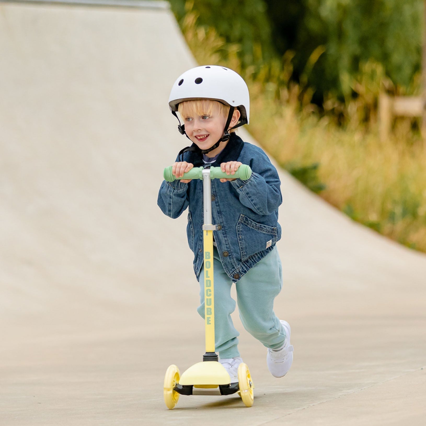 Child riding a yellow scooter on a path with greenery in the background