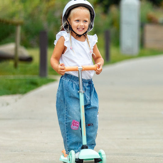 Child riding a scooter with a helmet on a paved path in a park.
