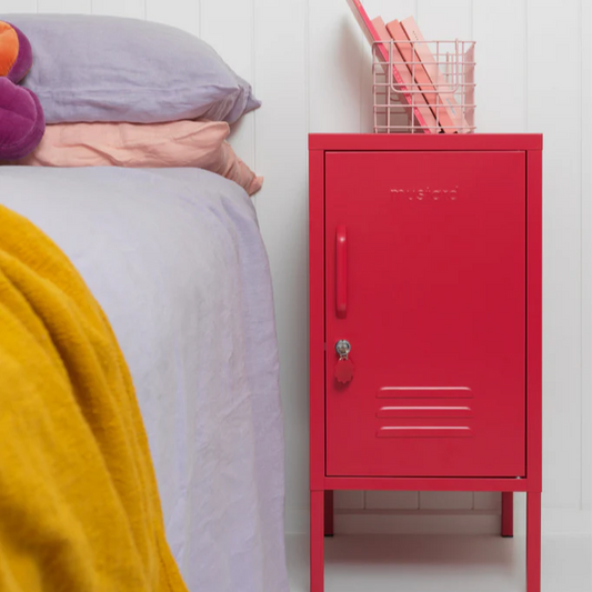 Red locker-style cabinet next to a bed with colorful bedding and a decorative flower poster on a white wall.