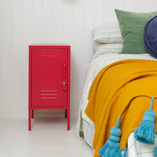Red locker-style cabinet next to a bed with colorful bedding and pillows.