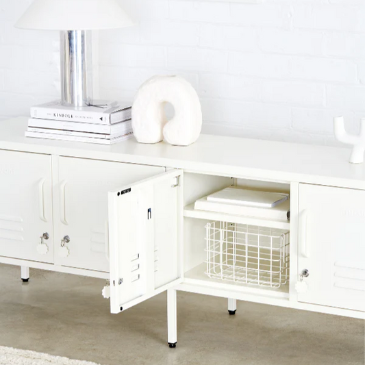 White cabinet with open door revealing a basket inside, on a light wooden floor.