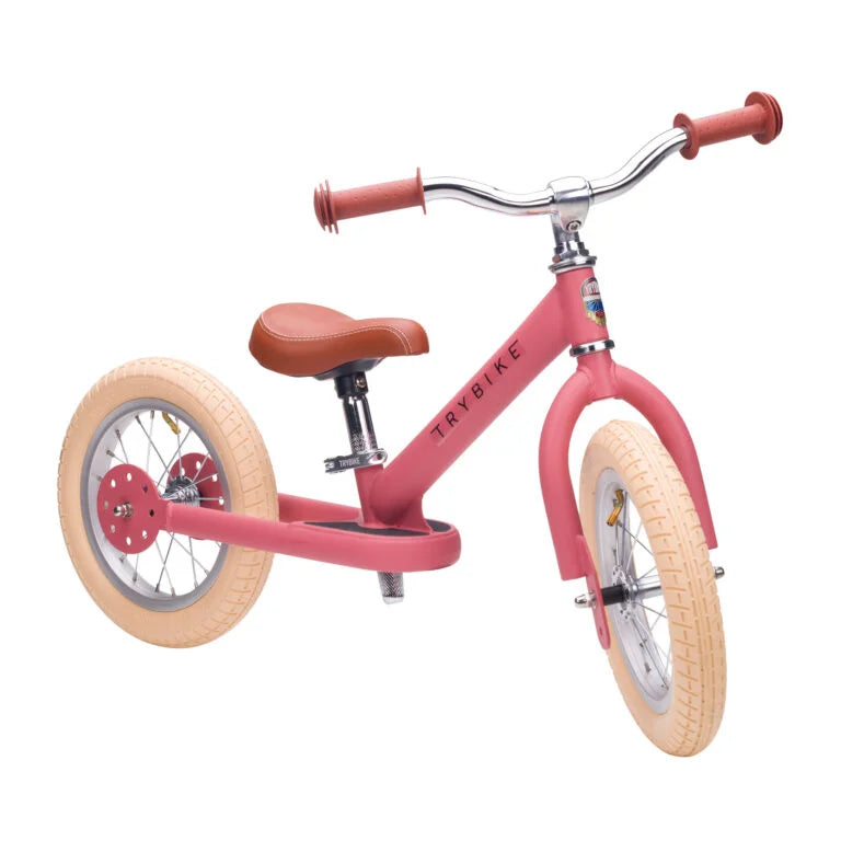 Pink balance bike with brown seat on a white background