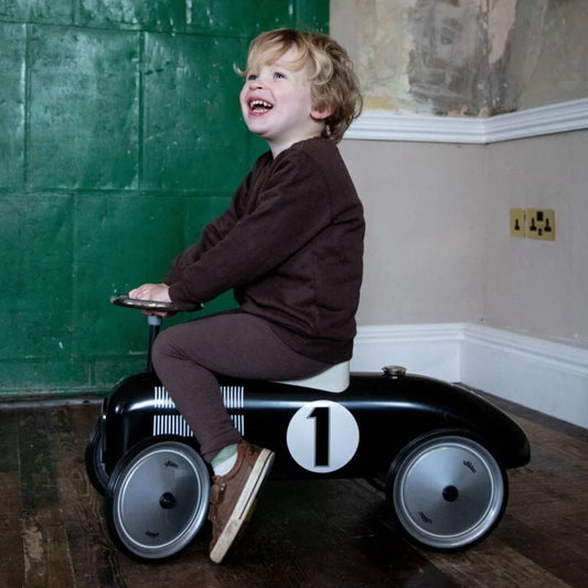 Black toy race car with number 1 on a wooden floor against a green wall with child on it