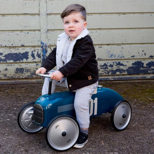 Child sitting on a blue toy car with a rustic background