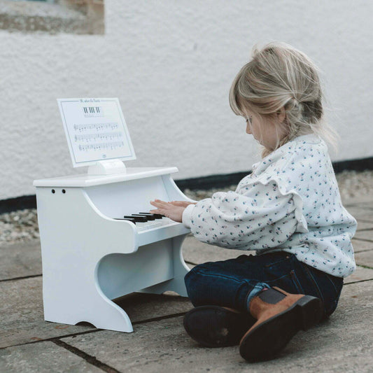 Child outside playing a white toy piano