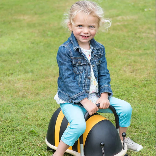 Child sitting on a toy vehicle in a grassy area