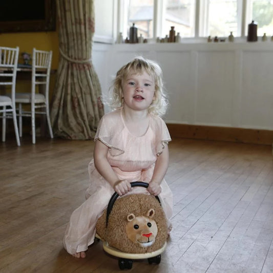 Child sitting on a lion-shaped toy in a room with wooden floor and white walls.