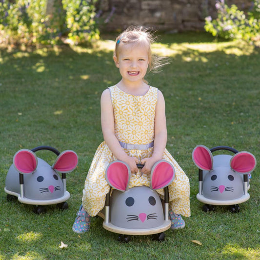 Young girl sitting on a mouse-shaped toy car in a grassy outdoor setting