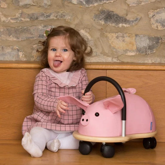 Child with a pink toy car shaped like a pig in front of a stone wall.
