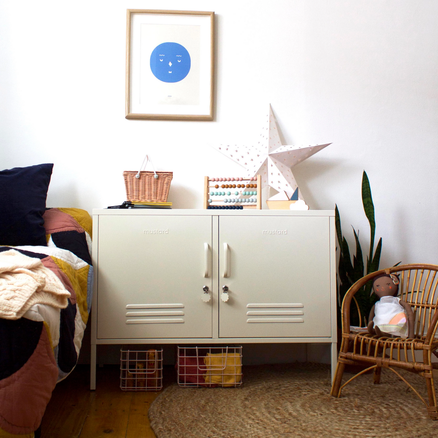 Nursery room with white cabinet, framed picture, and wicker chair.
