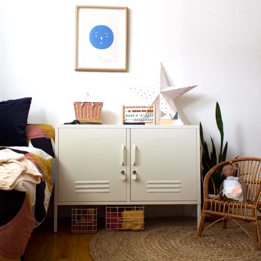 Nursery room with white cabinet, framed picture, and wicker chair.
