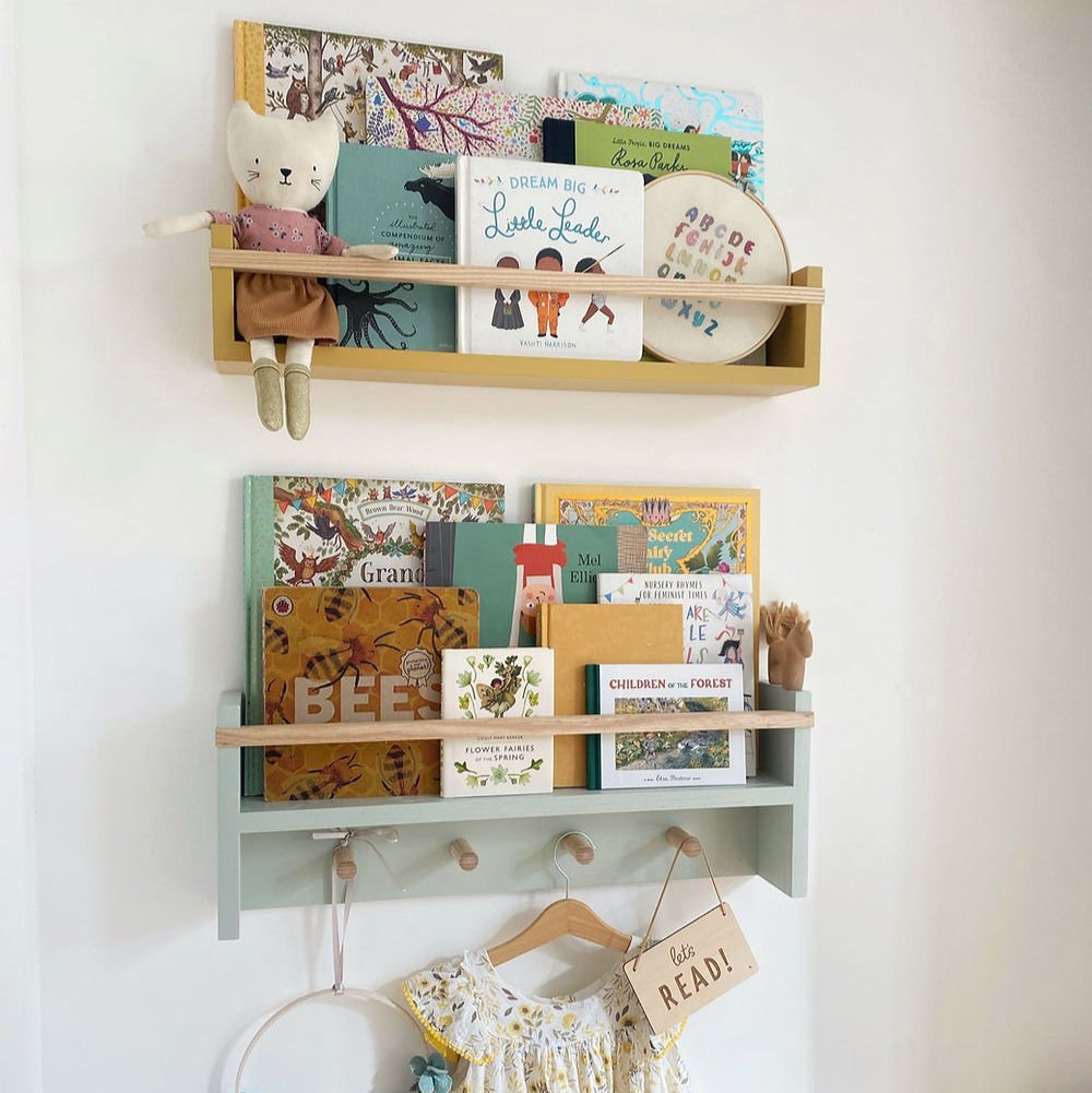 Wall-mounted shelves with books, toys, and a dress on a white wall