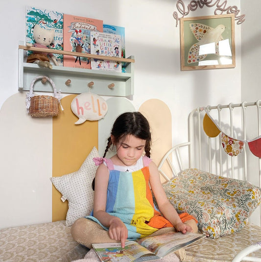Child sitting on a bed reading a book in a cozy bedroom with decorative elements.