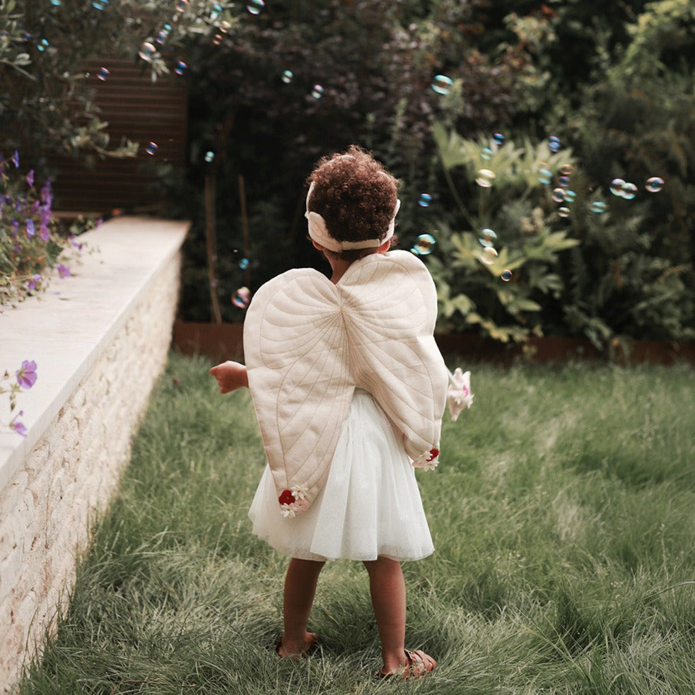 Child in angel costume with wings standing in a garden with bubbles