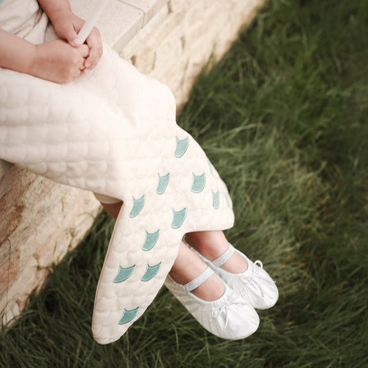 Child wearing white tights with blue owl patterns and white shoes sitting on grass.