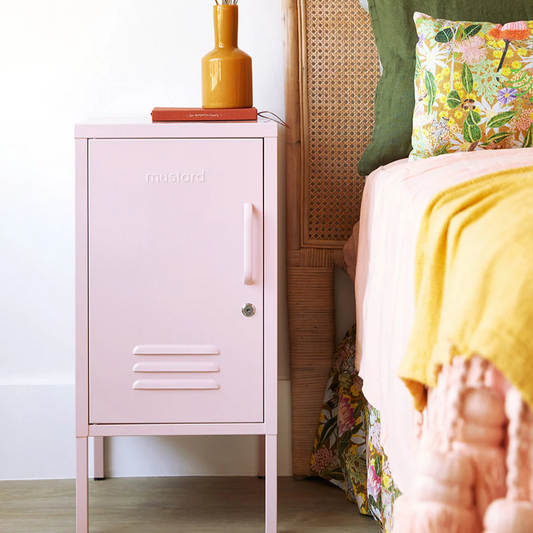 Pink locker-style nightstand next to a bed with floral bedding and green headboard.