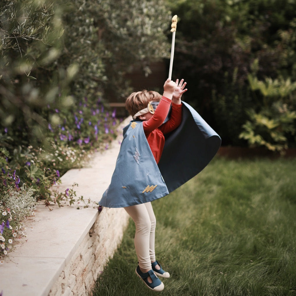Child in a blue dress and red sweater swinging on a swing set in a garden.