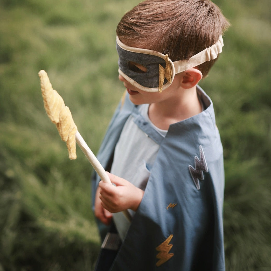 Child in superhero costume holding a toy spear with a blurred green background
