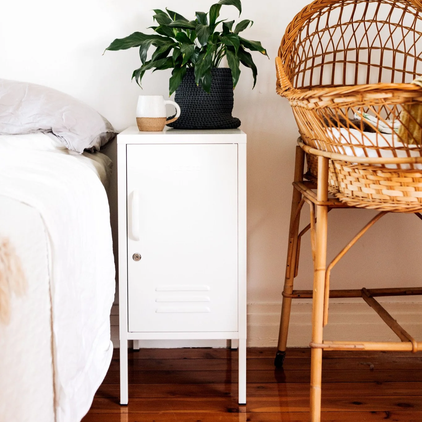 Bedroom with a bed, nightstand, plant, and wicker chair.