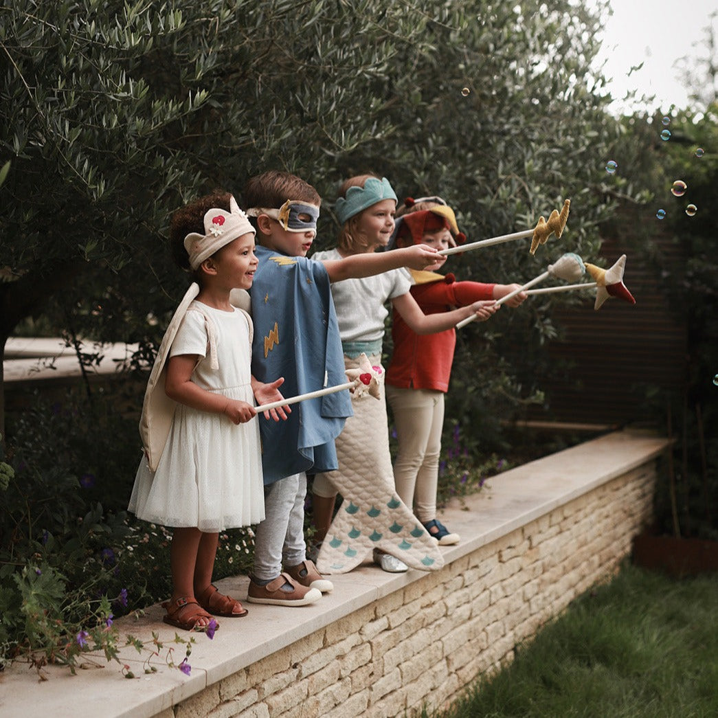 Children playing with toy brooms on a stone ledge outdoors.