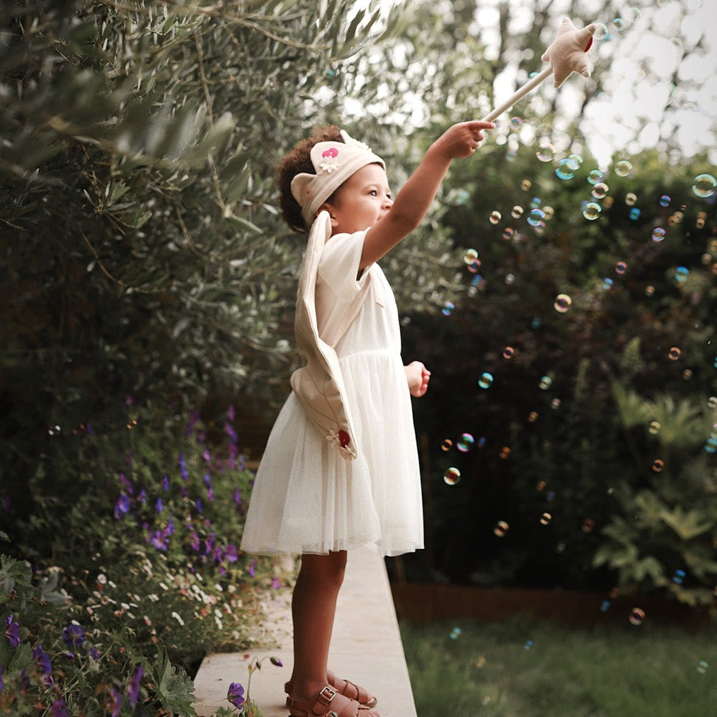 Young girl in a white dress blowing bubbles in a garden setting