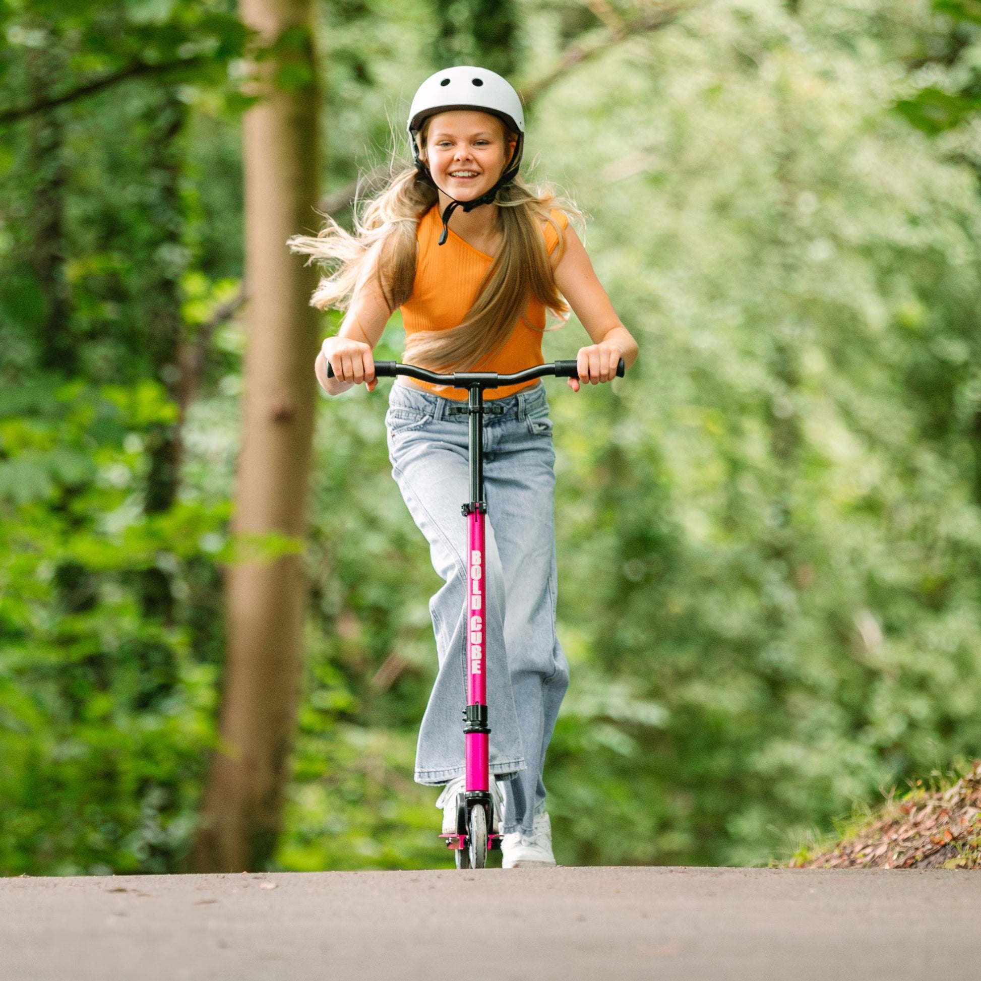 Young girl riding a pink scooter in a forested area