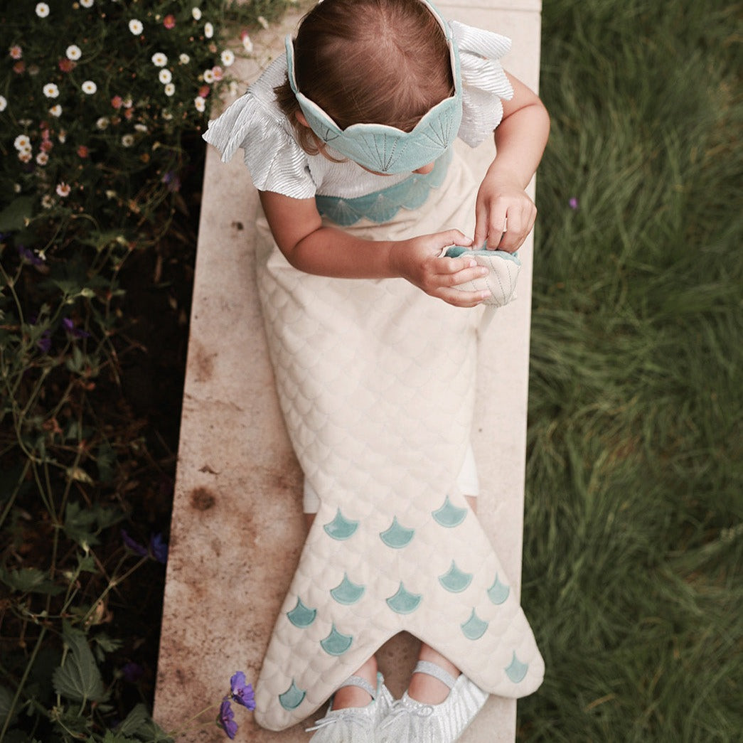 Child wrapped in a white blanket with blue patterns, standing outdoors.