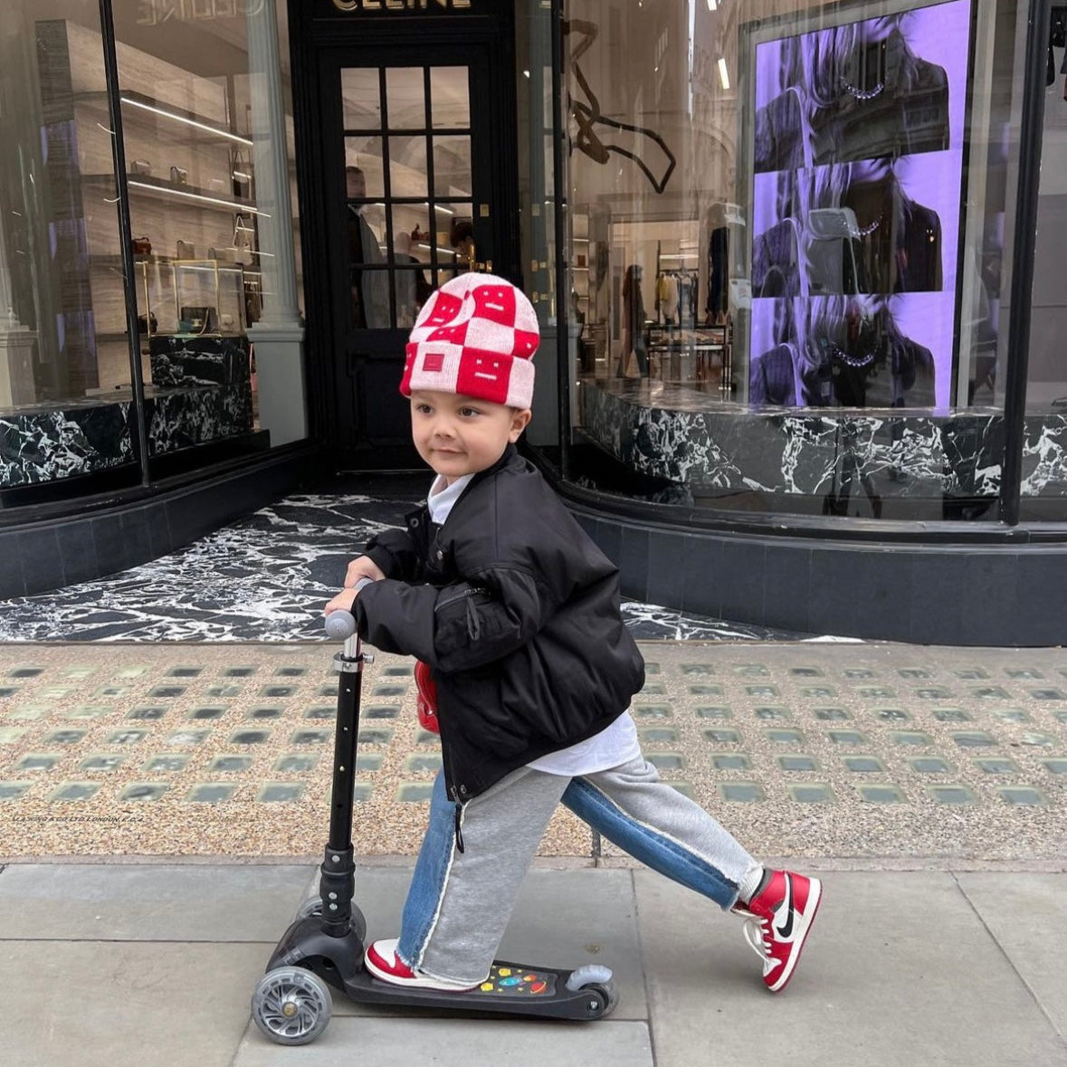 Child on a scooter in front of a Celine store