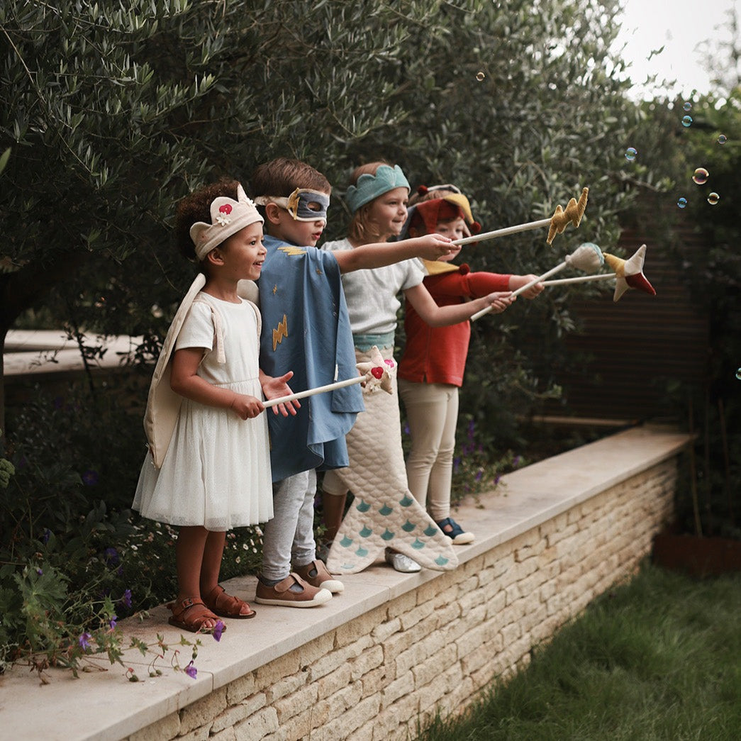 Children in costumes playing with bubble wands on a stone ledge outdoors.
