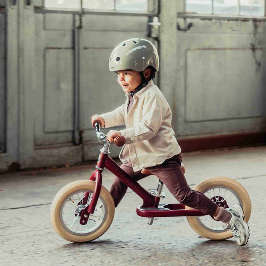 Child riding a balance bike with a helmet in an indoor setting
