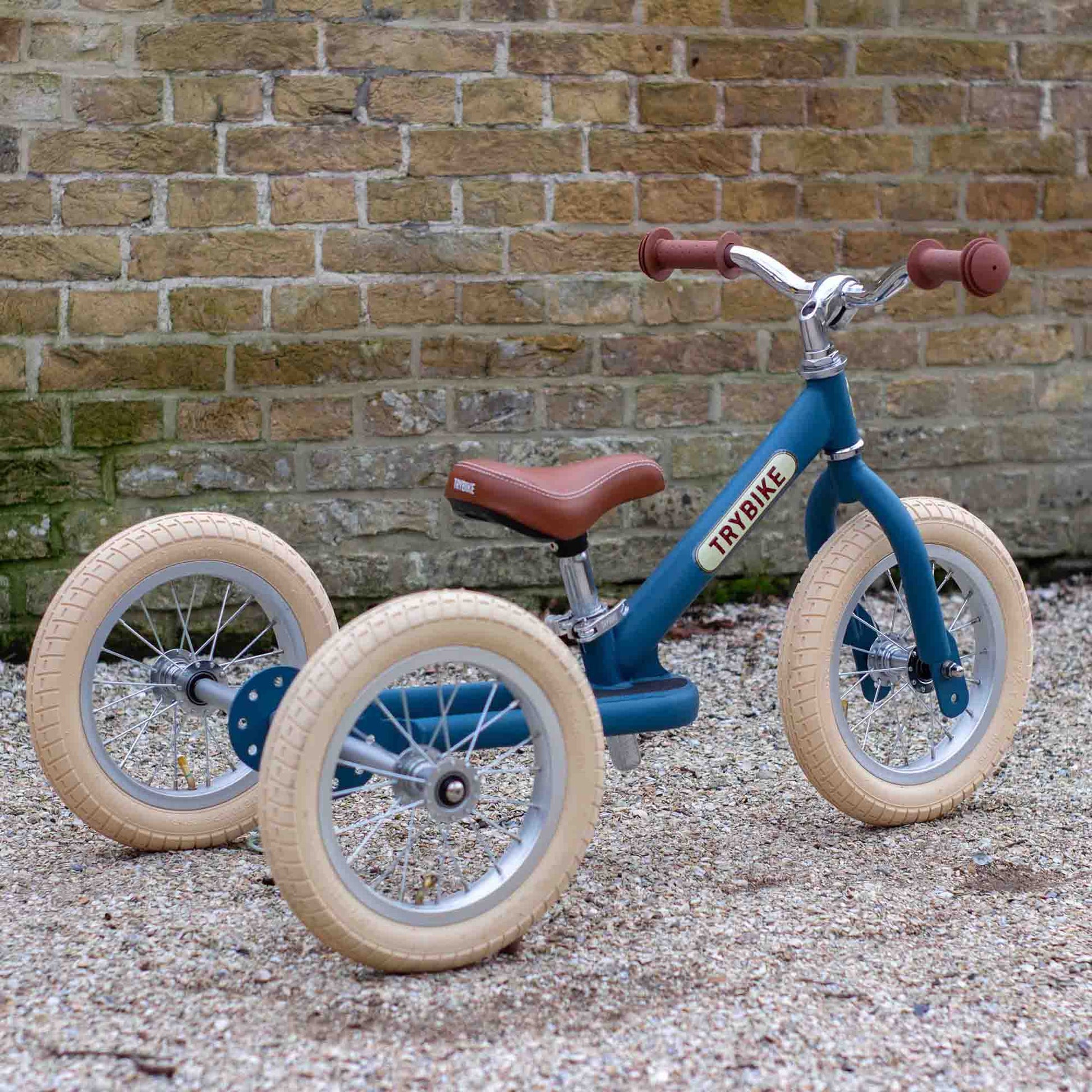 Blue balance bike with beige tires against a brick wall.