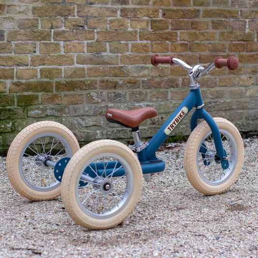 Blue balance bike with beige tires against a brick wall.
