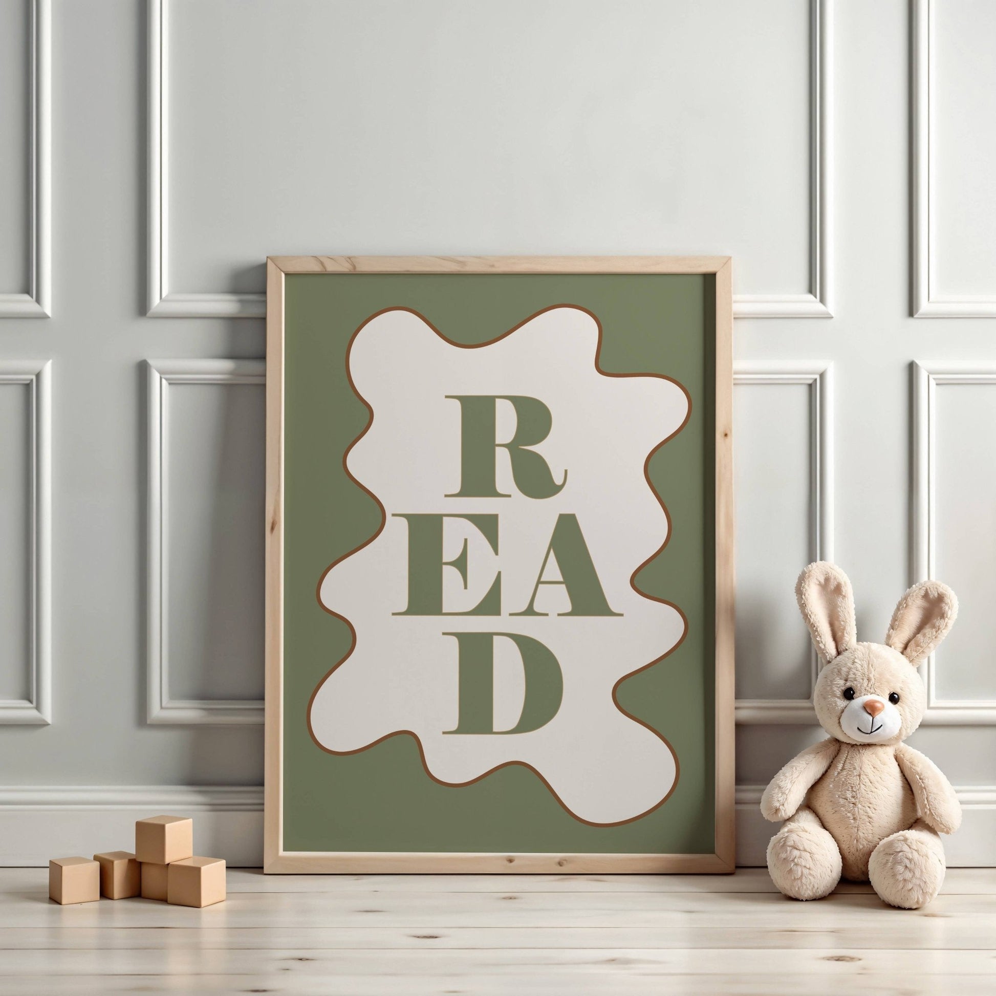 Framed poster with 'READ' text on a wall with a teddy bear and wooden blocks below.