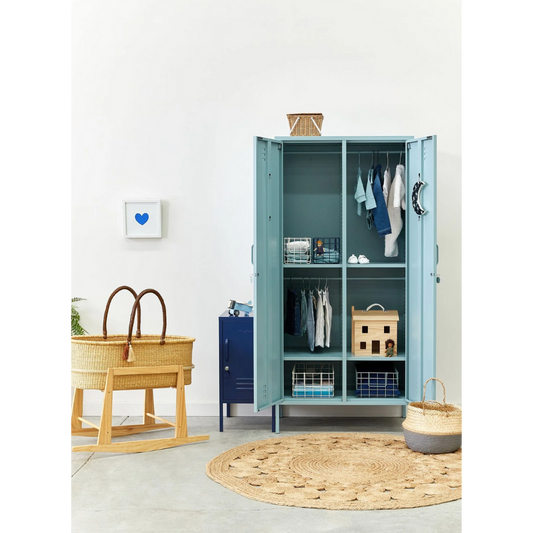 Blue wardrobe with open doors in a room with a bassinet and round rug.