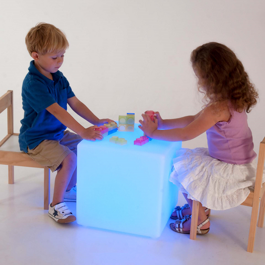 Two children playing with a glowing cube table on a white background