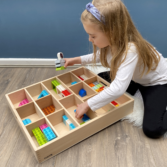 Child playing with colorful building blocks in a wooden sorting tray.