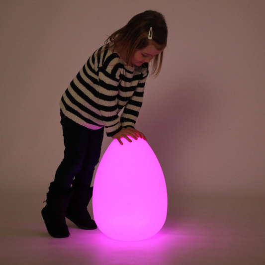 Child holding a glowing pink egg-shaped light against a plain background