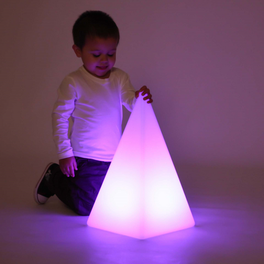 Child holding a glowing pyramid-shaped senosry light against a plain background