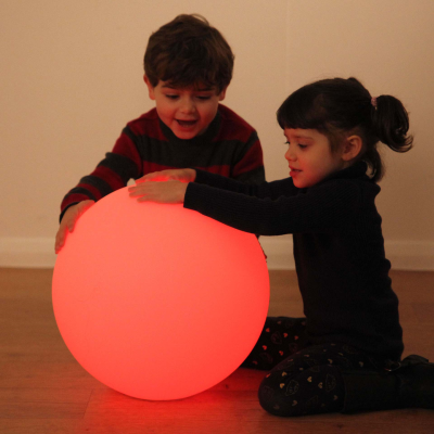Two children playing with a glowing red ball light on a wooden floor.
