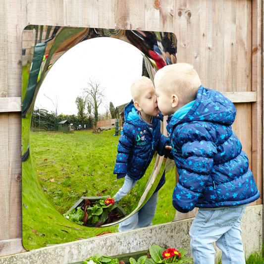 Child in a blue jacket  playing with mirror dome in an outdoor setting