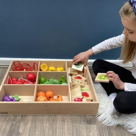 Child playing with a wooden toy set on a wooden floor.